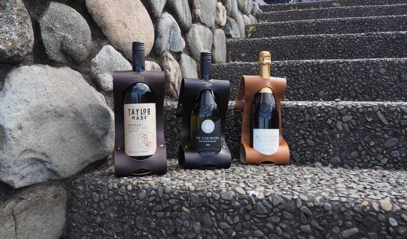 The three-piece sampler — tan, chocolate and black wine carriers together on stone steps