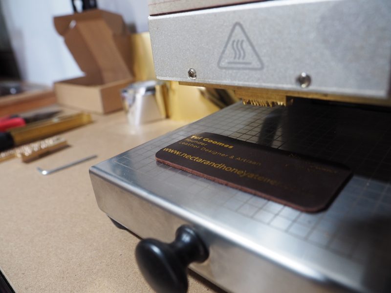 Tui hot-foil stamping the Nectar & Honey Atelier maker's mark onto a leather tag in the workshop